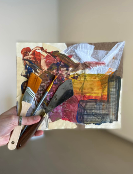Une main tenant une petite œuvre abstraite sur carton, devant une exposition professionnelle. 